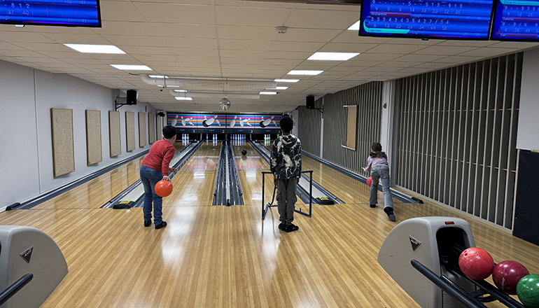 Tre barn som bowlar på varsin bana, fotograferat bakifrån.