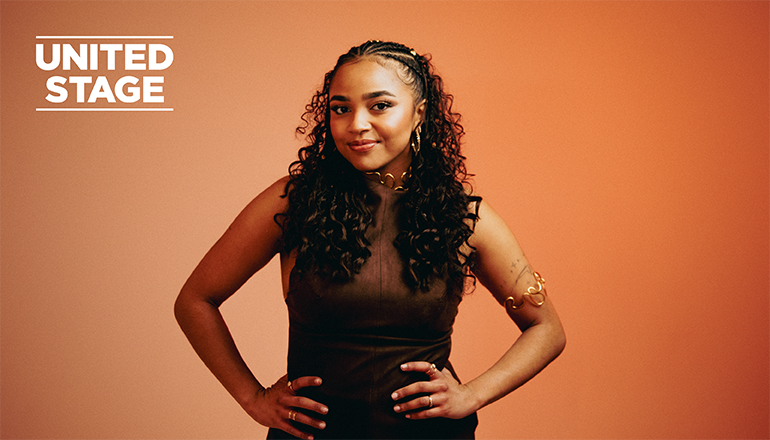 Porträttbild av mörkhårig ung kvinna mot orange bakgrund.