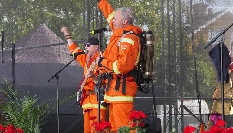 Två män i branduniform på en scen och sjunger.